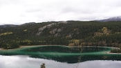 A placid lake alongside a woodsy hillside on an overcast day