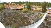 A suspended pedestrian bridge leads to a large wooden visitors center