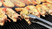 Hileras de langostas bañadas en mantequilla sobre una parrilla y una pinza con una de ellas en la mitad