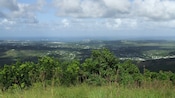 Vista do topo de uma colina de uma paisagem repleta de casas e sombras de nuvens que se estendem até o oceano