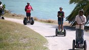 2 teenage boys follow a guide on Segway PTs by the ocean