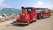Un tranvía diseñado para parecer una antigua locomotora a vapor estacionado junto a una bahía con cruceros