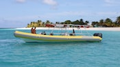 A rigid hull inflatable boat carrying 4 passengers anchored at a white sand beach