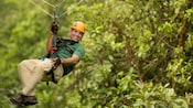 A man smiles as he hangs from a zip line in a forest