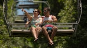 A couple sits in a ski lift chair over a forest
