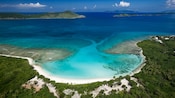 A white sand beach with Guests relaxing on beach recliners and a resort in the distance