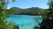 Montañas cubiertas de árboles se alzan imponentemente sobre una laguna transparente donde dos buzos exploran el agua