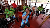 Una banda en vivo entretiene a las personas cantando y tocando tambores metálicos dentro de un barco