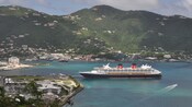 A Disney Cruise Line ship is docked close to the island shore