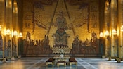A golden mosaic depicting a queen adorns an entire wall of a Byzantine style hall