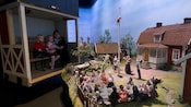 A mother and her 2 kids view a museum exhibit of miniature townspeople looking at a child on a flagpole