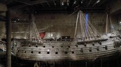An ancient looking sailing ship sits in a large warehouse