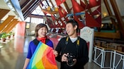 Smiling people holding a kite and a camera inside a building with a vaulted ceiling