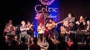 People hold hands in front of a stage with performers playing the drums, violins, guitars and keyboard