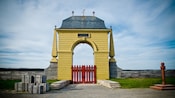 A gated archway topped with fleurs de lis overlooking a body of water
