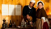 A woman dressed in a bonnet and an apron smiles as a man lifts a glass to a keg
