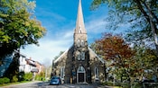 A compact car parked in front of a stone church museum featuring a single spire