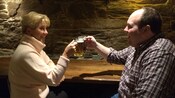 A woman with pale ale clinks mugs with a man who is drinking dark beer