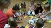 Children gather on the floor around an activity with stickers and drawings