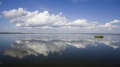 A calm body of water with clouds reflecting on the waters surface