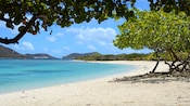 A white sand beach with calm waters and hills in the distance