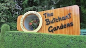A wooden sign above a manicured hedge reads The Butchart Gardens, Over 100 Years in Bloom