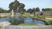 Manicured grounds featuring a fountain, greenery, benches, pathways and stone walls