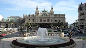 Two circular fountains surrounded by flowers sit in line in front of a 3 story building