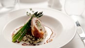 A plated fine dining entree featuring a stuffed meat roll on rice pilaf with asparagus 