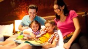Familia sonriente lee un libro en una cama de hotel con cabecera del Castillo de la Bella Durmiente