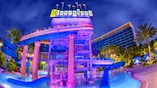 The Monorail waterslide and waterfall glow at night over the pool  area surrounded by hotel towers