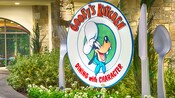 A giant fork, knife, spoon and plate featuring Goofys face and the restaurant name stand outside the entrance to Goofys Kitchen