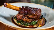 A lamb shank served atop sautéed spinach and parsnip puree