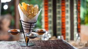 A cone-like metal holder with slices of crisp African breads and 3 dipping sauces