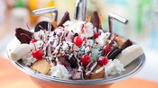 Un tazón con forma de lavaplatos lleno de helado, galletas, caramelos, pastel, crema batida y frutas