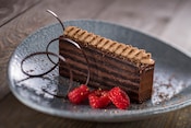 A piece of chocolate cake near 3 raspberries and a twist of chocolate