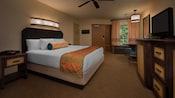 Una cama King Size de estilo caribeño frente a una cómoda con TV y una mesa redonda y, más allá, una puerta y una ventana