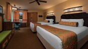 Deux grands lits sur le thème des Caraïbes, Commode avec TV, meuble à bagages, table ronde et, au-delà, une porte et fenêtre