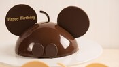 A chocolate cake designed to resemble Mickey Mouse, inscribed with the message 'Happy Birthday'