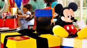Caixas de presente com embalagem colorida e um grande Mickey de pelúcia sentado na tampa
