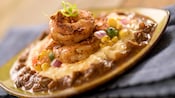 A plate topped with grits, sauce, corn, onions and shrimp