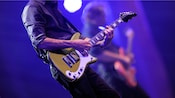 A guitarist performs on stage in the foreground alongside a fellow musician playing a bass guitar