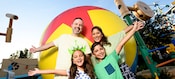 A mom and dad posing with their son and daughter in front of a big yellow Toy Story Ball designed to make guests appear the same size as toys.