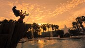Estatua de Mickey el brujo parado sobre la Piscina Fantasía en Disney's All-Star Movies Resort al atardecer