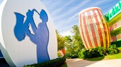 Circular structure with a saxophone player's silhouette across a path from a giant drum adorning the side of Disney's All-Star Music Resort