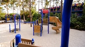 Un área de recreación arenosa con un juego para trepar, tobogán, redes y barras de mono en Disney's All-Star Music Resort