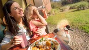 Una familia sonriente comiendo en una mesa de un restaurante mientras la hija juega con un par de binoculares
