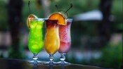 Three specialty drinks sitting on a wooden bar