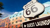 Une enseigne indiquant en anglais : « Services de buanderie » sous un panneau en forme de bouclier indiquant « Route 66 »