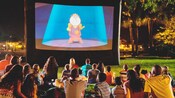Guests sit on grass and watch Beauty and the Beast at night